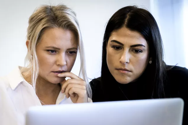Two female students looking into a computer screen. Photo.