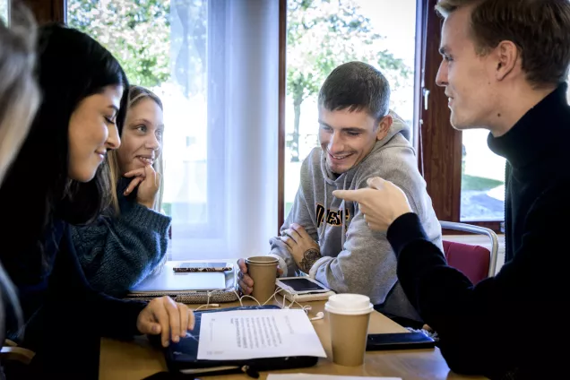 Fyra studenter i samtal kring ett bord. Foto.